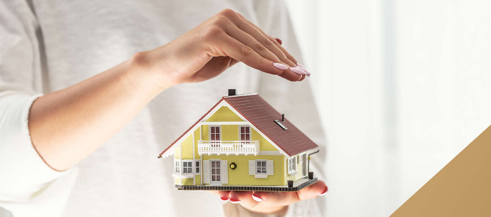 Woman holding a model house in her hand, sheltering it with her other hand as if protecting it.