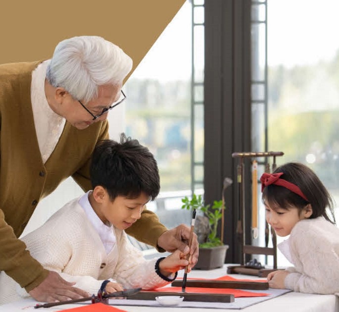 Grandpa passing on his knowledge of calligraphy to his grandson and granddaughter, as a metaphor for wealth and time-tested values.